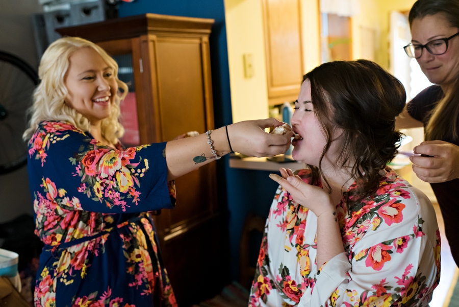 A bridesmaid feeds the bride a snack while she gets ready.